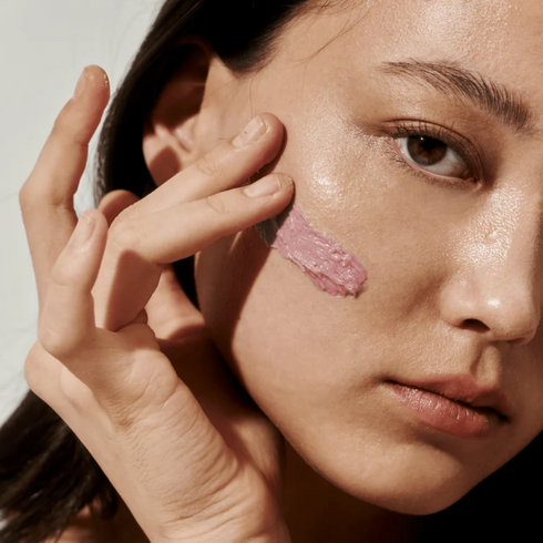 Close-up of a person applying pink makeup to their cheek with a neutral background