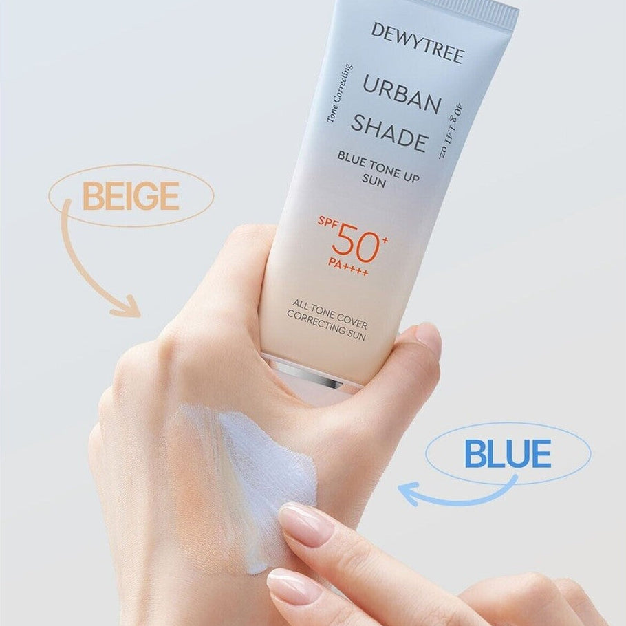 Dewytree Urban Shade Blue Tone Up SPF 50+ sunscreen tube held over a hand showing beige and blue swatches with labeled arrows.
